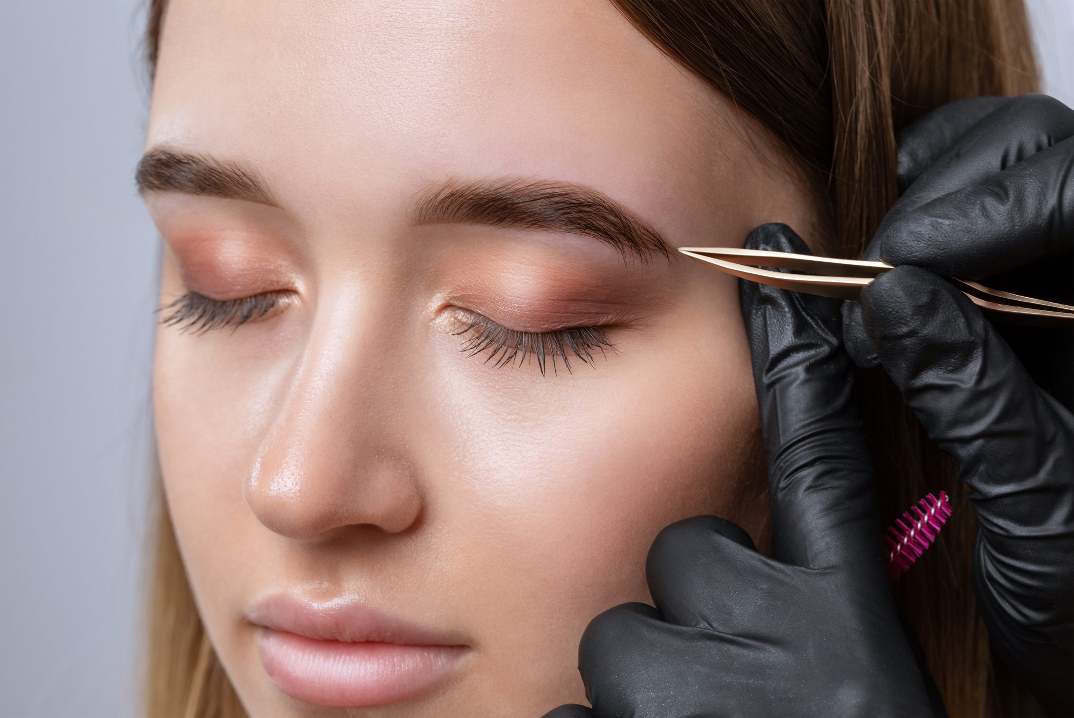 Woman having eyebrows tweezed by gloved hands