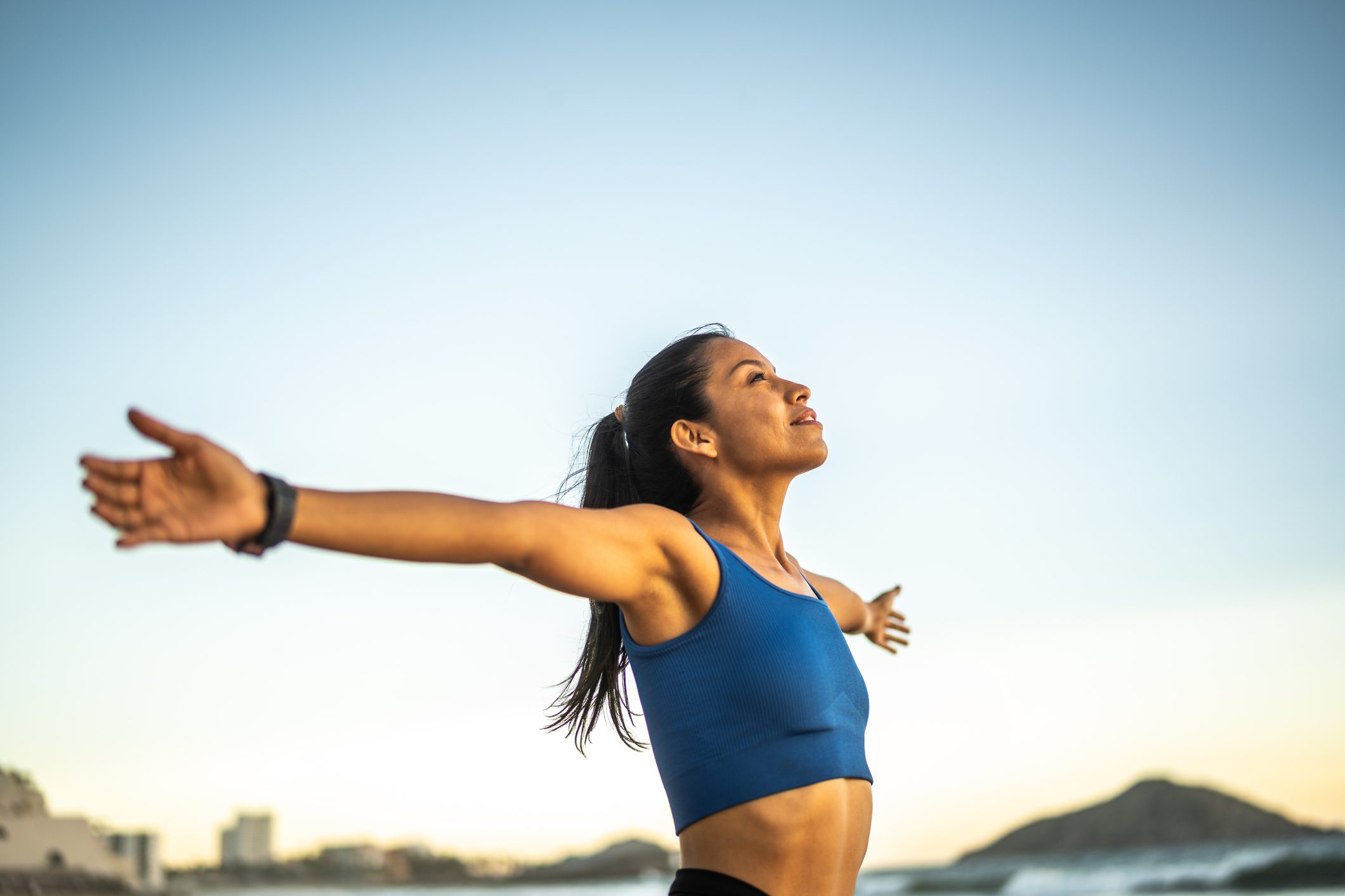 Woman in sportswear stretching arms outdoors with a serene expression.