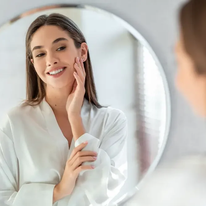 Young woman applying skincare cream in front of mirror.